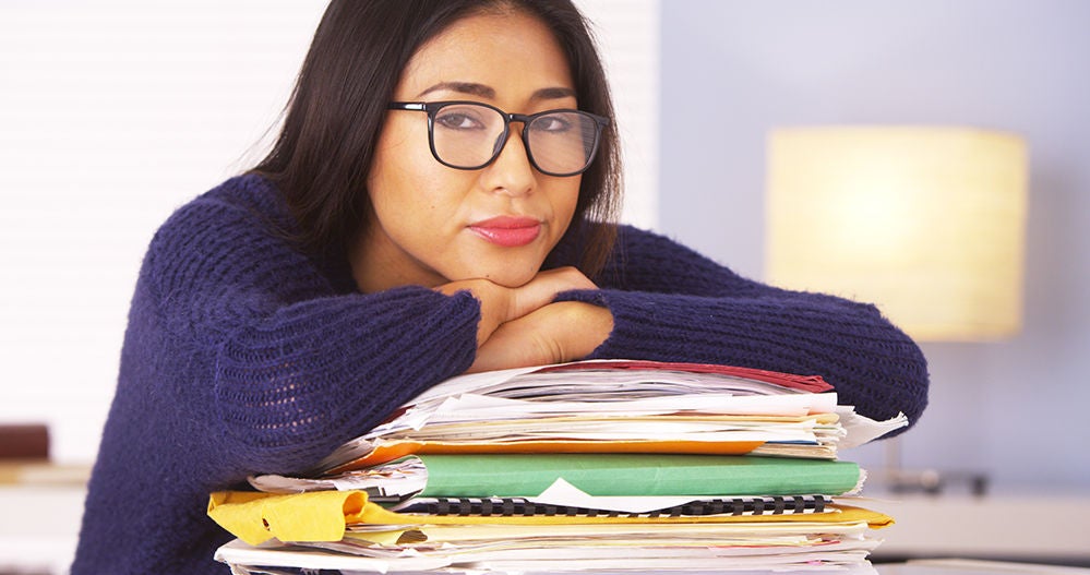 Person with their head resting on top of a stack of paperwork and folders