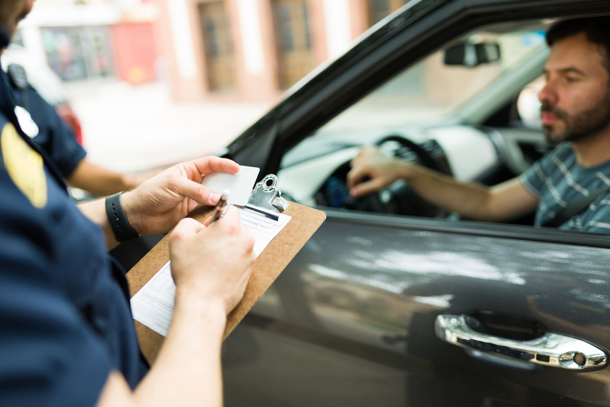 Close up of a police cop writing a traffic ticket or fine to a male driver in his car for speeding