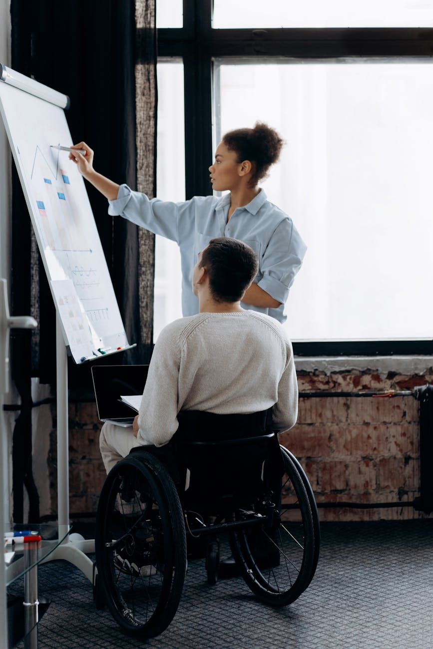 A woman and writing on a white board while a man in a wheelchair looks on