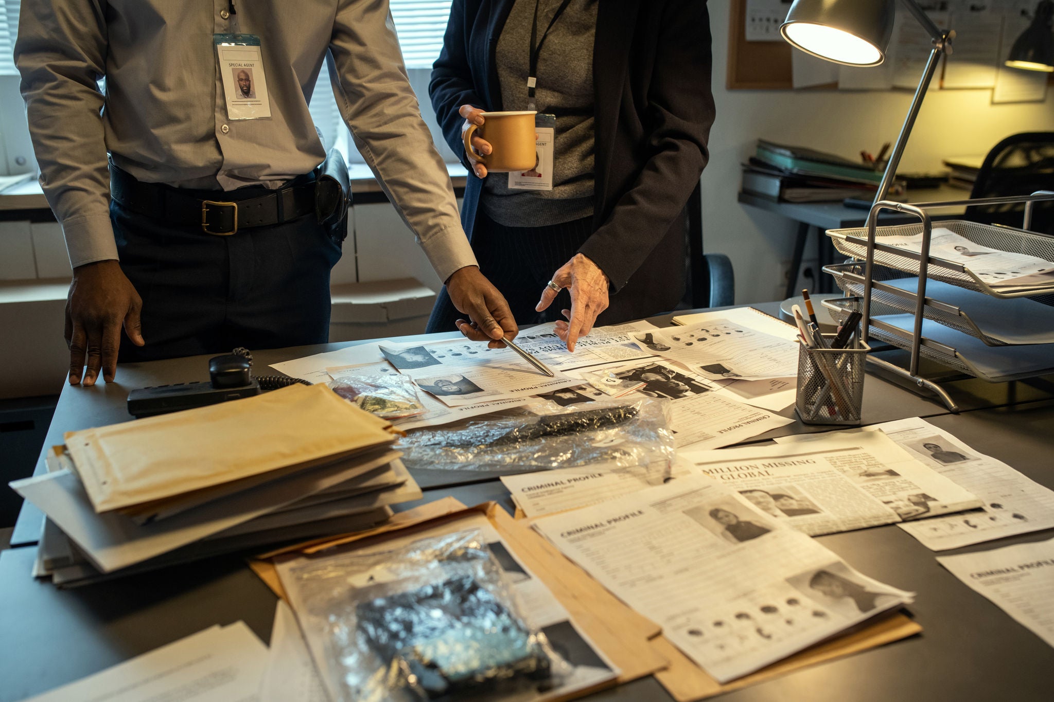 Two interracial agents of FBI pointing at personal information of gang leader while discussing criminal profiles during investigation