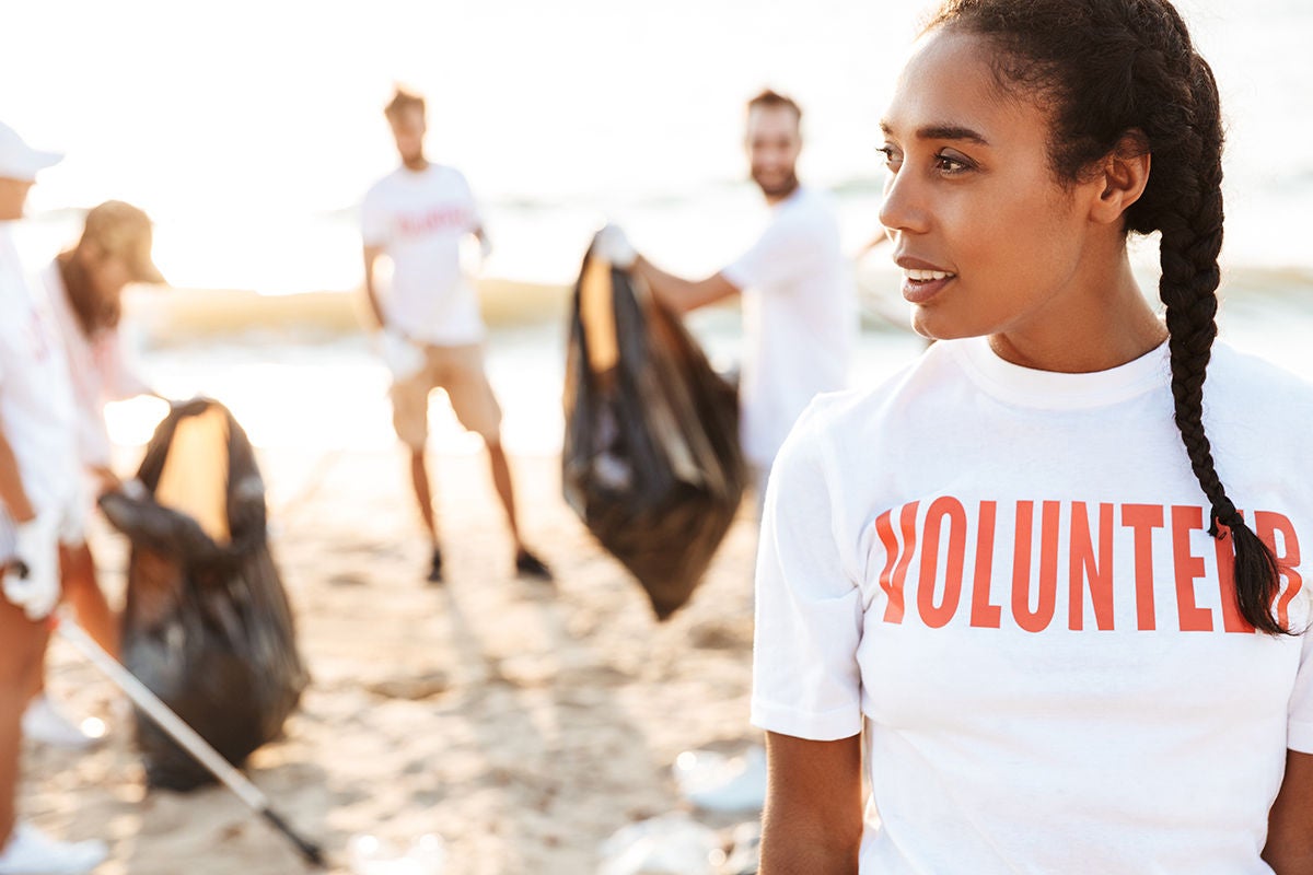 Photo of pleased female volunteer cleaning beach from plastic with trash bags at seaside