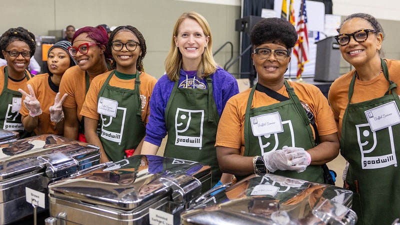 Comptroller Lierman with a group of volunteers all wearing green Goodwill aprons standing in front of  serving trays.
