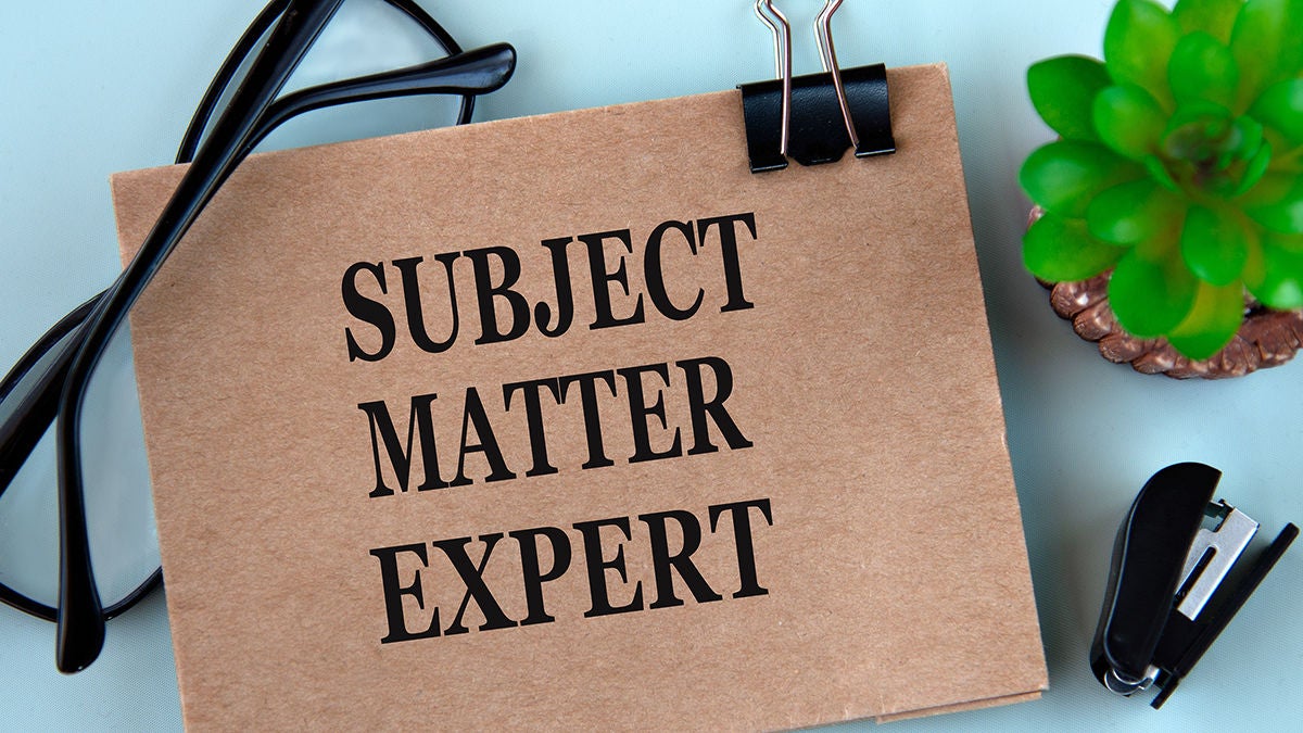 SUBJECT MATTER EXPERT words on brown paper on a light background with glasses, cactus and stapler