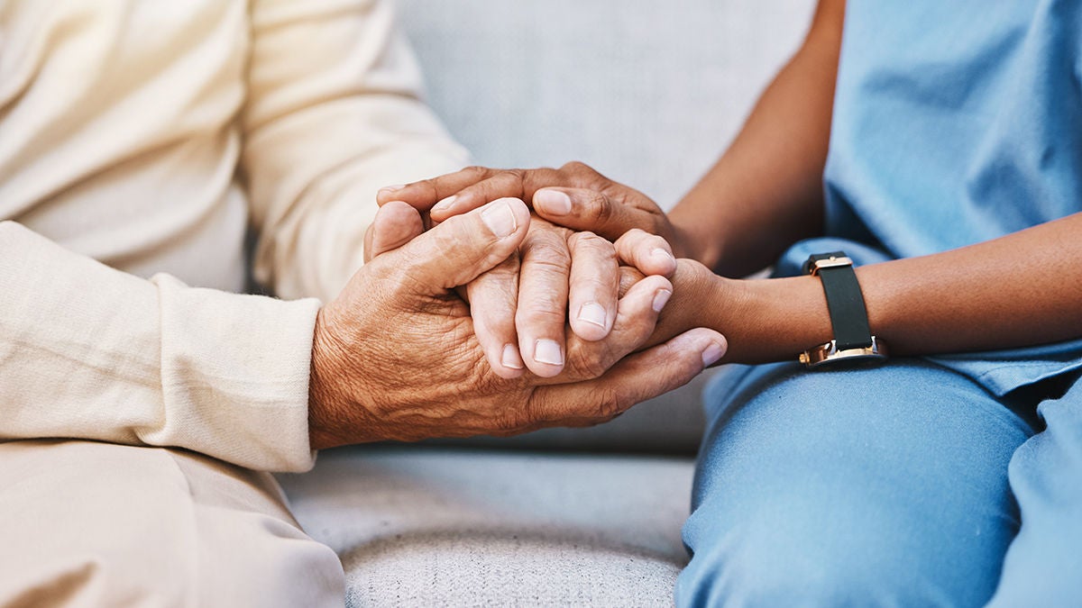 A close-up of an elderly man and a medical professional woman holding hands.