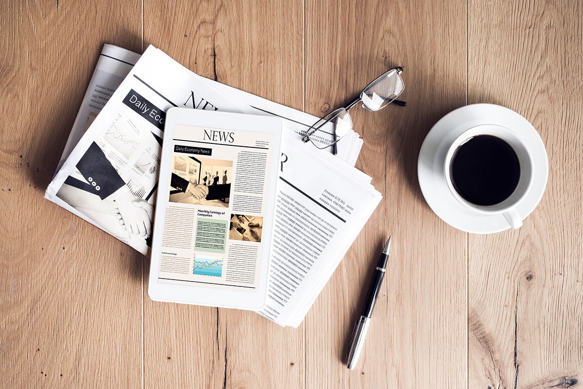 Newspaper with a tablet, cup of coffee, pen and eye glasses on wooden table