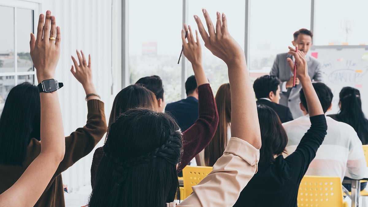 Audience raising hands up while businessman is speaking in training at the office.